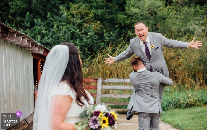 Photo by: <a href="https://www.wpja.com/contests/2018-v19/best-wedding-photographers/2377881">Andrea Bibeault - Omaha Nebraska</a> Nebraska Wedding Photograph of groom being carried away from his bride.