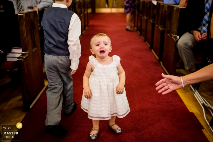 Photo by: <a href="https://www.wpja.com/contests/2018-v19-photography-competition/best-wedding-photographers/2380206">Ilana Bar-av - Madison Wisconsin</a> Eleva, Wisconsin wedding ceremony photograph of young girl crying in aisle by a Madison, WI wedding photographer