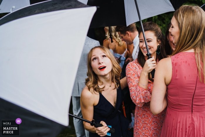 Photo by: <a href="https://www.wpja.com/contests/2018-v20-photography-competition/best-wedding-photographers/2386951">Rob Dodsworth - Norwich Norfolk</a> Wedding reception photography of guests with umbrellas in the rain | Norfolk weddings