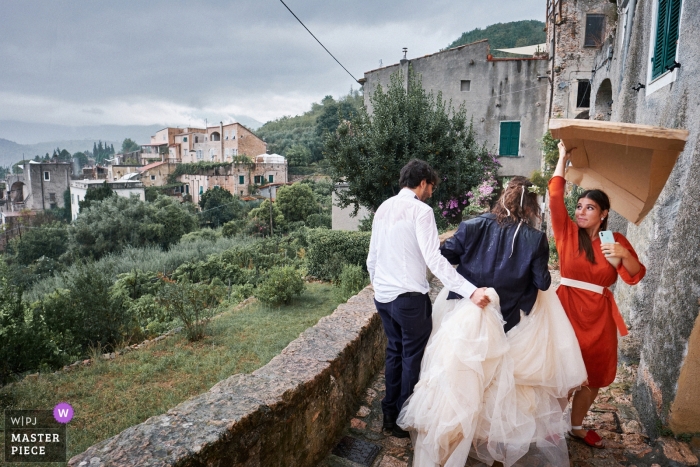 jour de pluie mariage à Savone | demoiselle d'honneur offrant un abri de la pluie pour la mariée