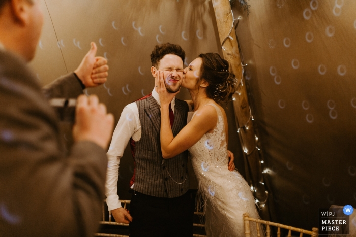 Fotografía de recepción de boda en Los Ángeles, California, de novia besando al novio en la mejilla a un invitado que responde con los pulgares arriba