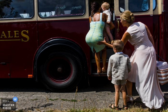 Trouwfoto in Vlaanderen van bruid die vriend helpt in de bruidsfeestbus