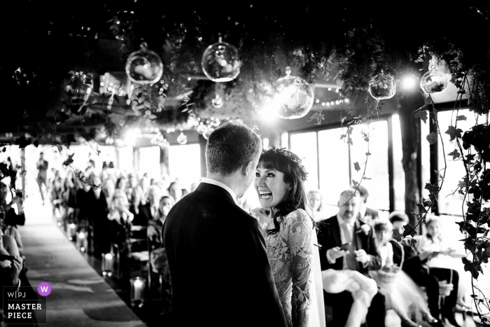 A beaming bride stands at the altar in Dewsall Court, Herefordshire, UK, in this stunning indoor wedding ceremony image in reportage-style Indoor Wedding ceremony at Dewsall Court, Herefordshire, UK