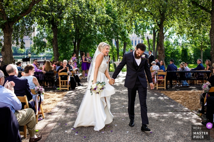 De fotografie van Chicago, Illinois van bruid en bruidegom die na openluchtceremonie onder de bomen opstappen