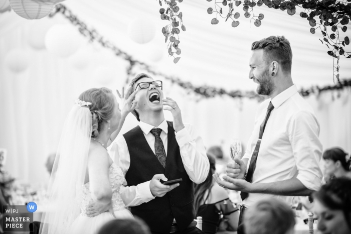 Foto: <a href="https://www.wpja.com/contests/2018-v20-Fotowettbewerb/Best-wedding-Fotografen/2409791"> Nick Despres - Guernsey Guernsey </a> Guernsey-Hochzeitsempfangsphotographie der Braut und des Bräutigams, die ein Lachen mit einem Hochzeitsgast teilen