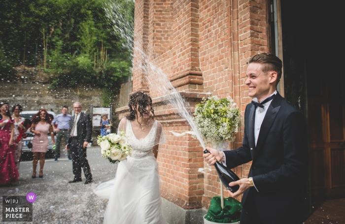 The bride ducked as the groom celebrated their union by spraying champagne outside the church after the wedding ceremony Turin wedding reception photography | groom spraying champaign outside church in Racconigi