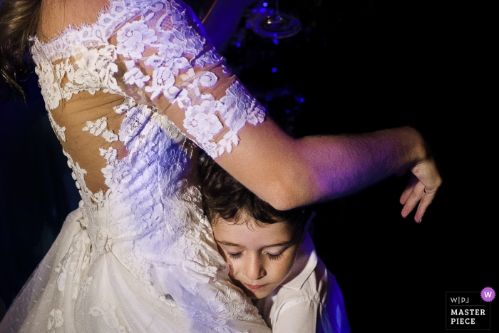 Photo by: <a href="https://www.wpja.com/contests/2019-v01/best-wedding-photographers/2426831">Clara Sampaio - Rio de Janeiro Rio de Janeiro</a> The bride gets a hug from a small boy at Tribuna B, Jockey, Rio de Janeiro, Brazil during the wedding party
