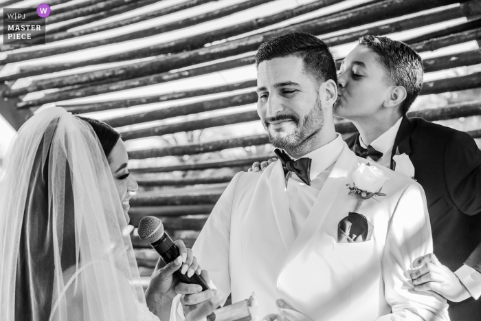 Photo: <a href="https://www.wpja.com/contests/2019-v01/best-wedding-photographers/2432096"> Alessandro Banchelli - Playa del Carmen Quintana Roo </a> Cérémonie de mariage au Royalton Riviera Cancun Resort - Le fils s'embrassant est papa pendant que la mariée parle dans un micro
