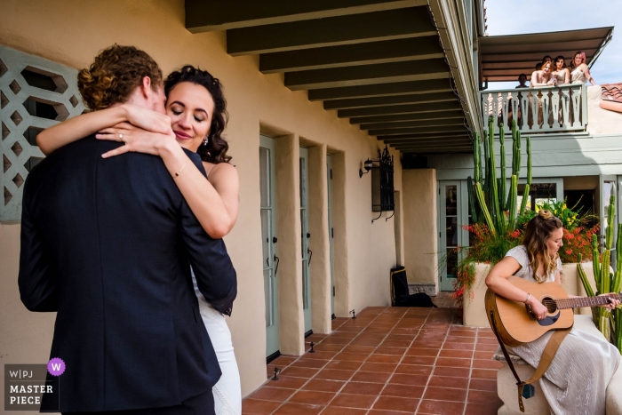 Foto door: <a href="https://www.wpja.com/contests/2019-v01/best-wedding-fotografen/2433641"> Shaunte Dittmar - Lake Tahoe California </a> O'donnell House Palm Springs, Californië - foto van de bruid en bruidegom omhelzen elkaar terwijl een bruidsmeisje een lied aan hen opdraagt