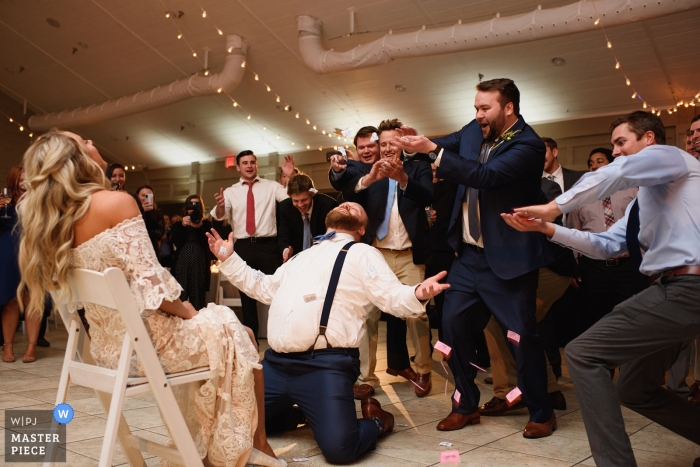 Photo by: <a href="https://www.wpja.com/contests/2019-v01/best-wedding-photographers/2437396">Neil Thurston - Nags Head North Carolina</a> Sanderling Resort, Duck, NC, wedding photographer - Groomsmen pour sugar packets on the groom as he removes the bride's garter.