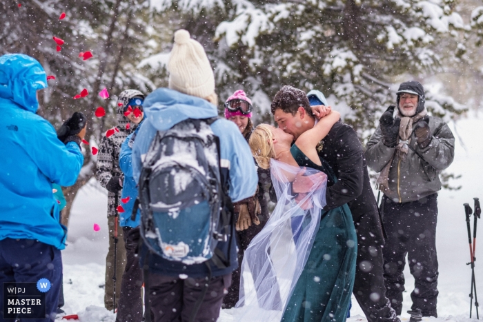 Photo by: <a href="https://www.wpja.com/contests/2019-v01/best-wedding-photographers/2437716">Annie Bang - Los Angeles California</a> Mammoth Lakes, California wedding photograph - The bride and groom kiss during their wedding ceremony in blizzard, surrounded their friends and family.