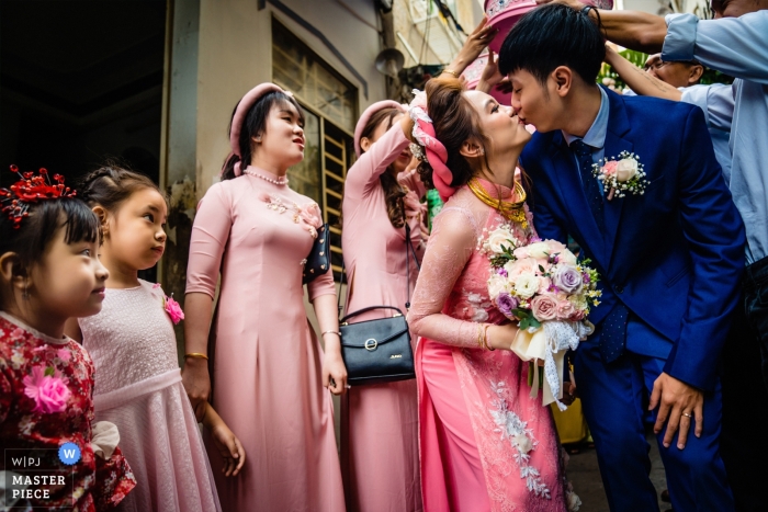 Foto por: <a href="https://www.wpja.com/contests/2019-v02/best-wedding-photographers/2442101"> Vu Nguyen - Ho Chi Minh </a> Rituales del día de la boda de Vietnam Cantho: rostros sorprendidos de los niños y la pareja que se besan afuera