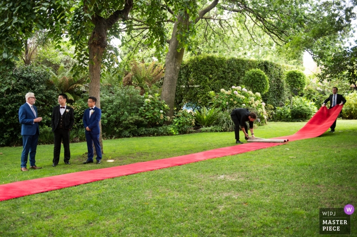 Hochzeitsfotograf aus Melbourne – Vorbereitung des langen roten Teppichs im Gras für die Zeremonie im Freien – Braut auf dem Weg