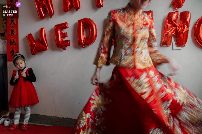 Photo by: <a href="https://www.wpja.com/contests/2019-v04/best-wedding-photographers/2466011">Su Xu - Fuzhou </a> The bride twirls in her red wedding gown as a young girl watches in this photo by a Fujian, China wedding photographer.