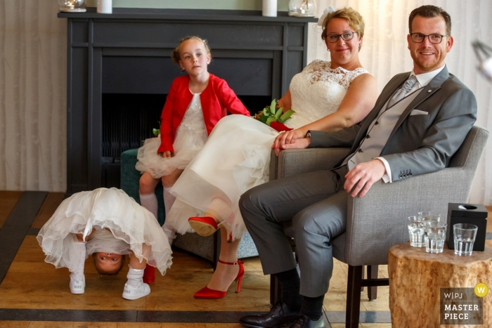 Photo by: <a href="https://www.wpja.com/contests/2019-v04/best-wedding-photographers/2467441">Indra Simons - Enschede Overijssel</a> A young girl gets another point of view of the wedding as she peeks between her legs while the bride, groom, and another young girl pose for this portrait by a Hellendoorn, Netherlands wedding photographer.