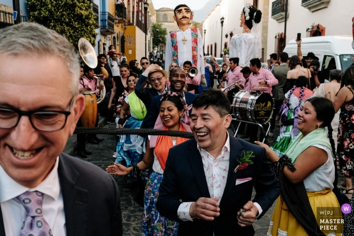 Die Brautparty und die Gäste machen ihren Weg durch eine Calenda oder Oaxacan Street Parade, auf diesem Foto von einem Hochzeitsfotografen aus Mexiko.