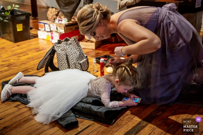 The flower girl lays on the floor getting her hair done at the Chicago-Bridgeport Art Center in this photo by a Chicago, IL wedding photographer.