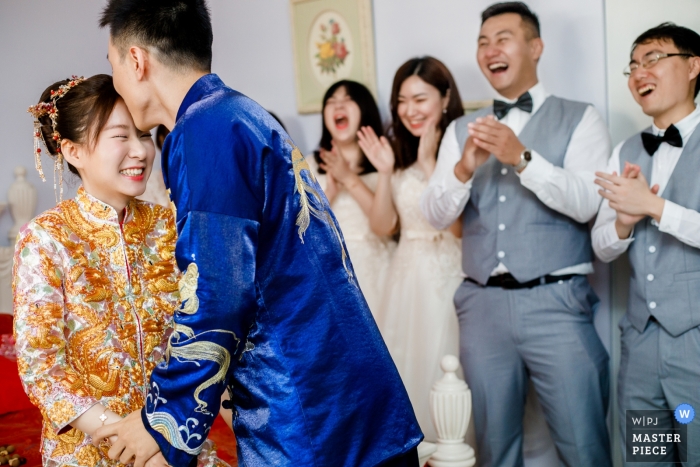 Photo by: <a href="https://www.wpja.com/contests/2019-v04/best-wedding-photographers/2469016">Miller Yao - Hangzhou </a> wanda hotel wuhan china | The groom kisses the bride as friends cheer for him on actual wedding day.