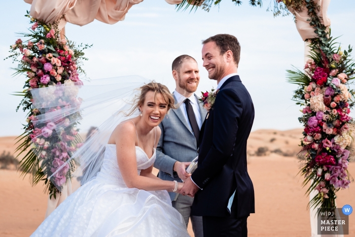 Photo by: <a href="https://www.wpja.com/contests/2019-v04/best-wedding-photographers/2469491">Bernie Richardson - Dubai </a> Al Maha Desert Resort Dubai Outdoor Ceremony in the Sand - Photo of the Brides reaction to the grooms joke