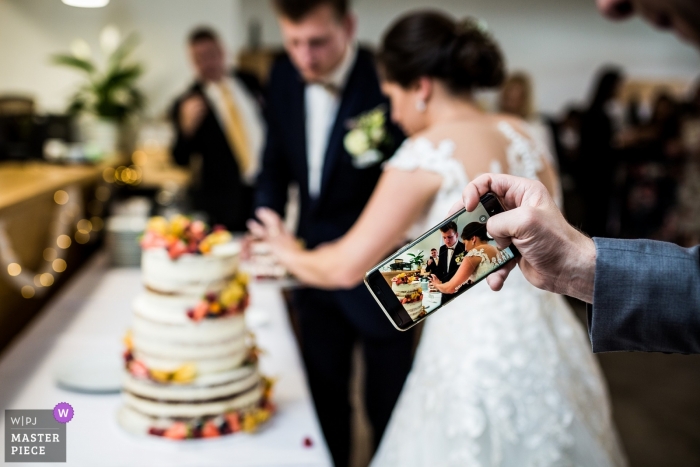Photo by: <a href="https://www.wpja.com/contests/2019-v04/best-wedding-photographers/2471016">Matouš Bárta - Prague </a> Pension on the Green Farm cake cutting photograph with guests phone camera incorporated in the shot.