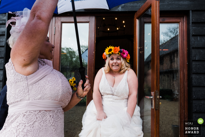 Colville Hall, Essex wedding day photography in the rain | Bride being sheltered from the rain 