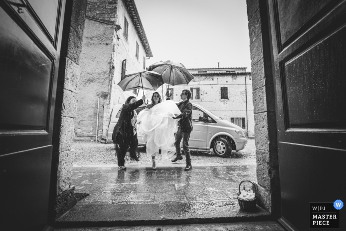 Foto door: <a href="https://www.wpja.com/contests/2019-v05/best-wedding-fotografen/2479046"> Andrea Sampoli - Siena </a> Abbadia Isola, Monteriggioni, Siena huwelijksfoto die de aankomst van de bruid onder de regen tonen