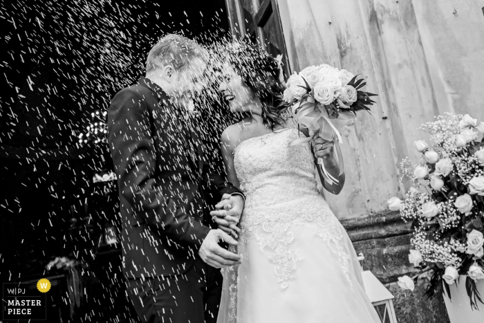 Foto door: <a href="https://www.wpja.com/contests/2019-v05/best-wedding-fotografen/2479716"> Luigi Rota - Comomeer Lecco </a> Lecco-trouwfotograaf heeft deze zwart-witfoto gemaakt van de bruid en bruidegom die met hun confetti bij hun ceremonie aan het Comomeer regenden