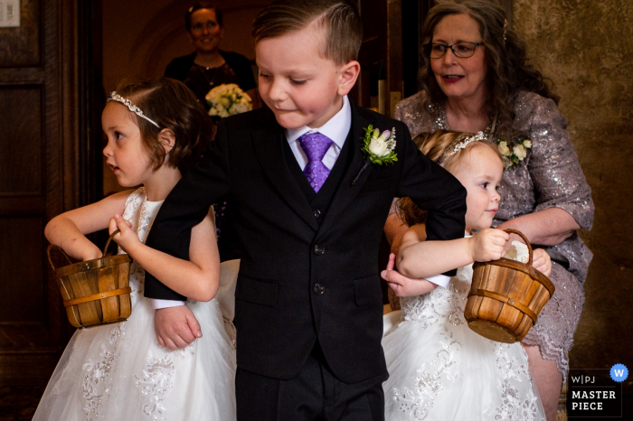 Fotografia de casamento em Edmonton mostrando o portador de anel ajudando as damas de honra pelo corredor