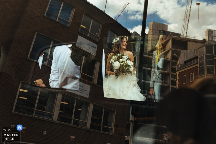 Photo by: <a href="https://www.wpja.com/contests/2019-v05/best-wedding-photographers/2482161">Lyndsey Goddard - London London</a> Vivo Islington Wedding Photography showing the Bride as she gets in wedding car as viewed through the window