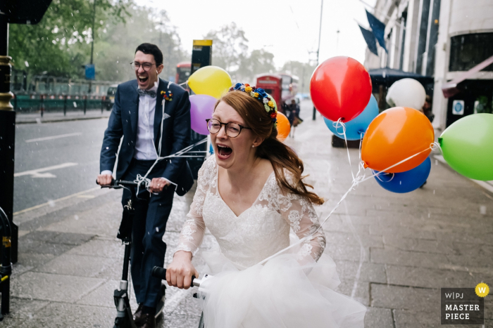 Photo by: <a href="https://www.wpja.com/contests/2019-v05/best-wedding-photographers/2482336">Kristian Leven - London</a> Royal Hospital Chelsea Wedding Photographer | The Bride + Groom encounter a hail storm as they scooter to the venue with balloons