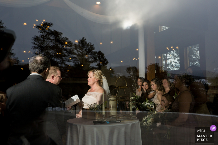 Foto por: <a href="https://www.wpja.com/contests/2019-v05/best-wedding-photographers/2483421"> Brenda Bergreen - Evergreen Colorado </a> Della Terra Mountain Chateau Fotógrafo de bodas | Imagen de la ceremonia de interior, mirando desde el exterior a través de la gran ventana de vidrio.