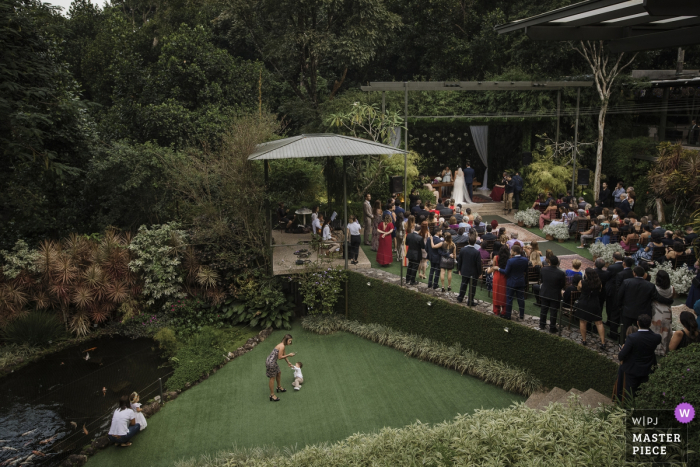 Imagen de la ceremonia de boda al aire libre de Casa das Canoas, Río de Janeiro, Brasil con niños jugando en el césped.