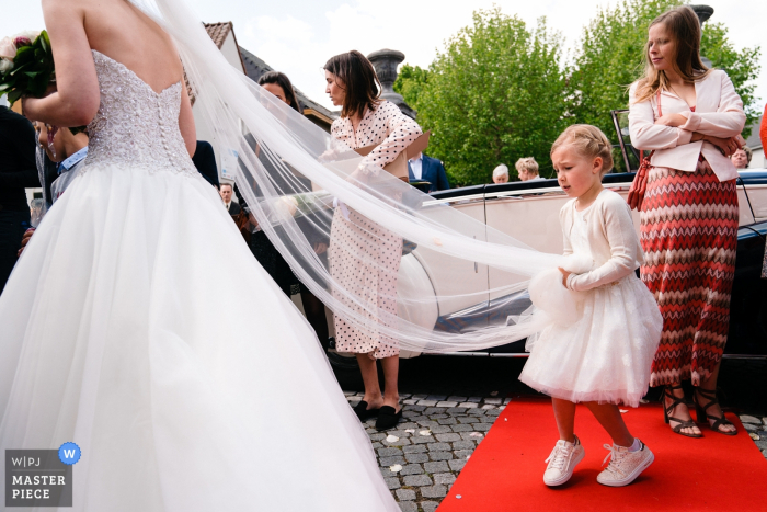 Flanders Church Photography showing the Little girl as she struggles with carrying the veil 