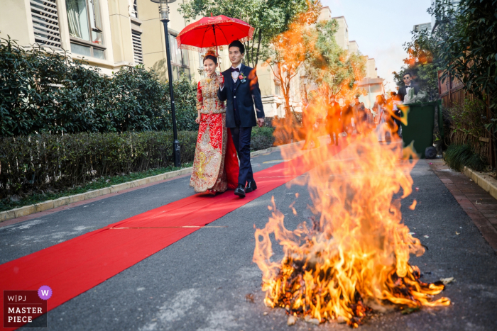 Foto: <a href="https://www.wpja.com/contests/2019-v06/best-wedding-photographers/2488311"> Mango Gu - Hangzhou </a> Die Braut und der Bräutigam gehen entlang einen roten Teppich draußen durch ein Feuer in diesem Hochzeitsbild, das von einem award-winning Hangzhou-Stadt, China-Fotografen gefangen genommen wird.