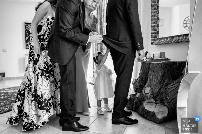 Foto von: <a href="https://www.wpja.com/contests/2019-v06/best-wedding-photographers/2492321"> Salvo Moroni - Viagrande Catania </a> Ein Trauzeuge hilft einem anderen Mann, sich fertig zu machen, während ein kleines Mädchen versucht, auch auf diesem Foto zu helfen, das von einem Hochzeitsfotografen aus Sizilien im Castello Xirumi di Serravalle aufgenommen wurde.