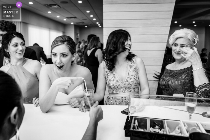 Foto von: <a href="https://www.wpja.com/contests/2019-v06/best-wedding-photographers/2492946"> JD Land - Marlton New Jersey </a> ICONA Avalon Hochzeitsempfang-Foto, das die Braut und ihre MOH / Schwester im Schock an ihrer Mutter zeigt, die geraden Whisky trinkt