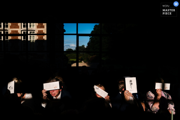 Photo by: <a href="https://www.wpja.com/contests/2019-v06/best-wedding-photographers/2493621">Yves Schepers - Bonheiden Antwerpen</a> Dinner guests are blinded by the evening light and use the menu cards to hide their eyes in this Kasteel Ter Block wedding ceremony photograph.