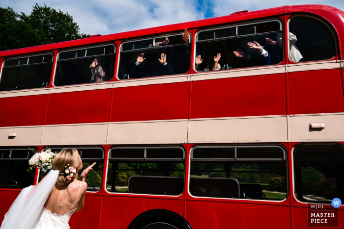 Foto di matrimonio a Kasteel Ter Block | La sposa soffia baci ai suoi ospiti che salutano che arrivano in un autobus di cerimonia