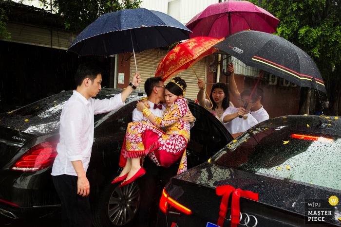 I testimoni dello sposo portano la sposa e tengono gli ombrelli su di lei per tenerla asciutta sotto la pioggia in questa immagine in stile documentario composta da un fotografo di matrimoni Huizhou, in Cina.