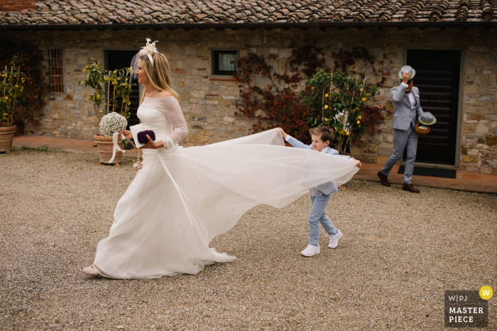 Foto von: <a href="https://www.wpja.com/contests/2019-v06/best-wedding-photographers/2493936"> Julian Kanz - Portofino Genova </a> Castello di Spaltenna, Toskana | Hochzeits-Foto, das den jungen Sohn hilft seiner Mutter mit ihrem Kleid zeigt