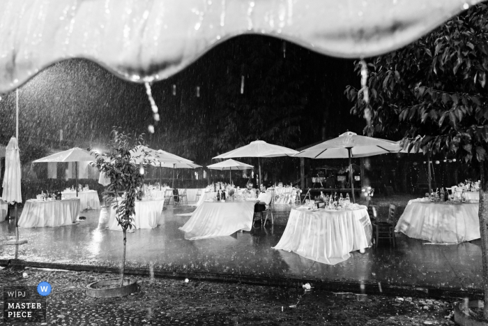 Zdjęcie: <a href="https://www.wpja.com/contests/2019-v06/best-wedding-photographers/2494946"> Matteo Reni - Busto Arsizio Varese </a> Puste stoły recepcyjne siedzą na zewnątrz w burzy w Cascina Pietrasanta na czarno-białym obrazie stworzonym przez fotografa ślubnego z Lombardii.