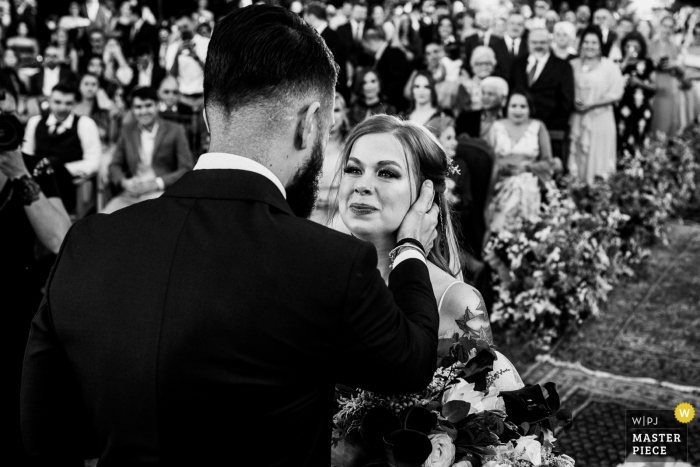 Gli sposi si fermano insieme all'altare durante il loro matrimonio a Vinicola Laurentia in questa foto in bianco e nero composta da un fotografo in stile documentaristico Rio Grande do Sul, in Brasile.