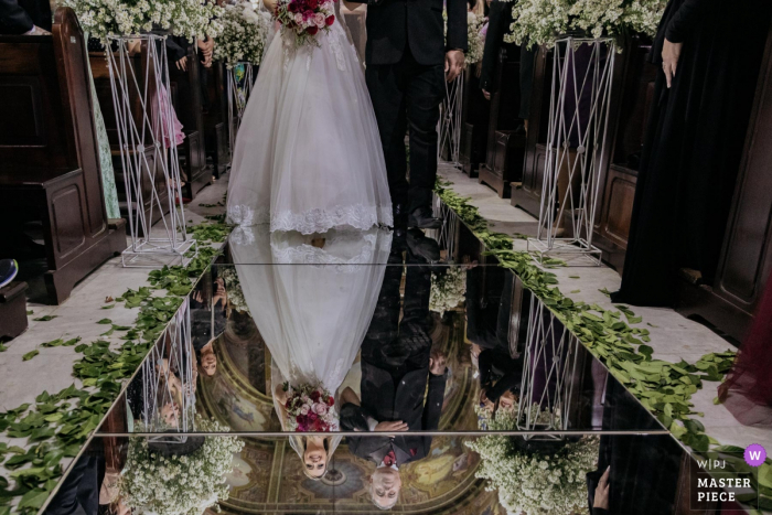 Photo by: <a href="https://www.wpja.com/contests/2019-v07/best-wedding-photographers/2499626">Eric Corbacho - São Caetano do Sul São Paulo</a> Ceremony Photograph Santo André Igreja Matriz do Carmo - The bride entering the church (in Brazil some brides choose these walkways of mirrors). detail of the contact with the father on the upper plane, and the smile on the bottom when seeing the groom