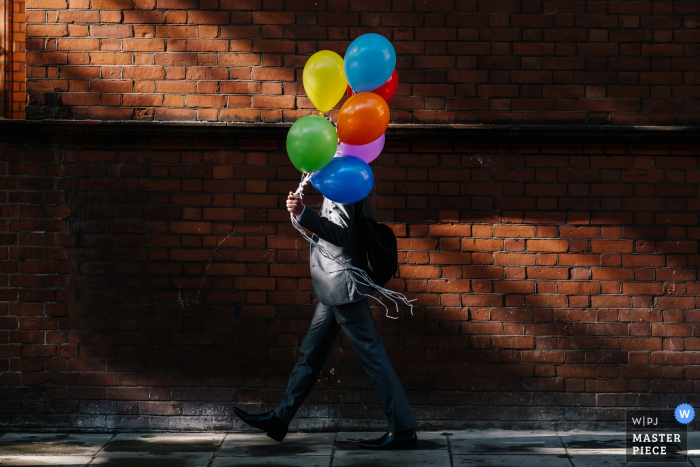 Photo by: <a href="https://www.wpja.com/contests/2019-v07/best-wedding-photographers/2499971">Kristian Leven - London</a> Royal Hospital Chelsea Wedding Photo as A Groomsmen walks past some lovely light with some colourful balloons