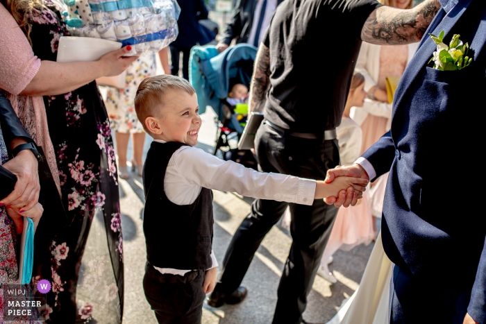 A boy gives a man a strong handshake after the ceremony at Parish of Bl. Władysława in Warsaw in this wedding photo created by a Lodz documentary photographer. 