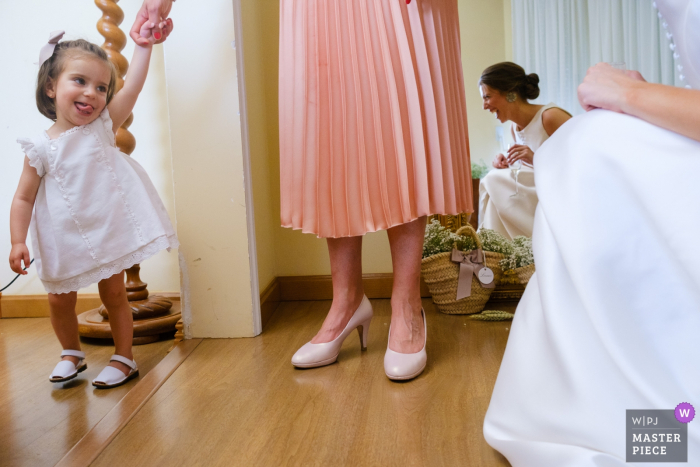 Une femme tient la main d'une petite fille tandis que la mariée s'agenouille et lui sourit avant la cérémonie à Alcoy sur cette photo de mariage réalisée par un photographe d'Alicante, Valence.