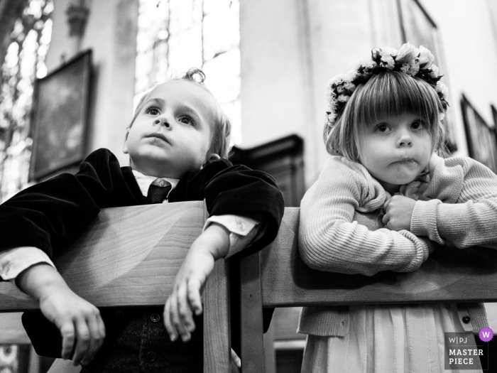 Photo by: <a href="https://www.wpja.com/contests/2019-v07/best-wedding-photographers/2504566">Joshua Dhondt - Antwerpen</a> A young boy and girl lean over the backs of their chairs in this black and white wedding photo composed by a documentary-style Antwerpen, Flanders photographer.