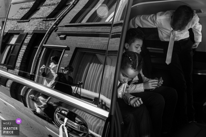 Photo by: <a href="https://www.wpja.com/contests/2019-v07/best-wedding-photographers/2504576">Joshua Dhondt - Antwerpen</a> Brick buildings are reflected in a car door as children prepare to exit the vehicle at De Lelie, Veurne in this black and white photo by an Antwerpen, Flanders wedding photographer.
