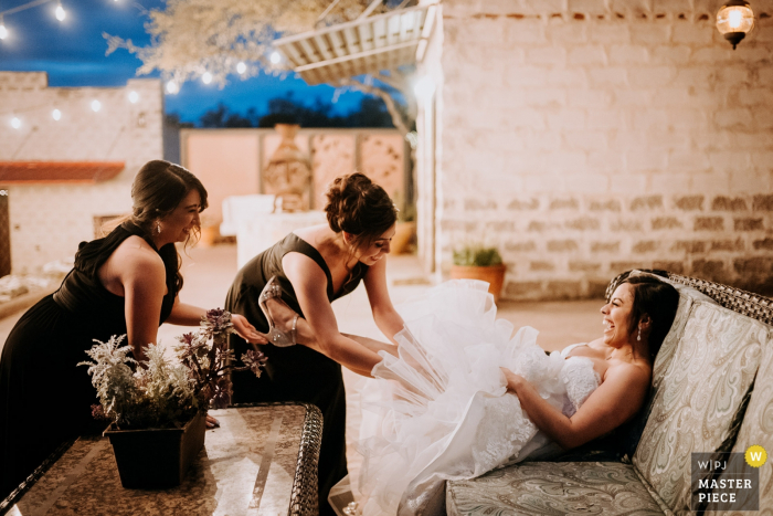 Foto por: <a href="https://www.wpja.com/contests/2019-v07/best-wedding-photographers/2504756"> Philip Thomas - San Antonio Texas </a> Helotes, Texas - The Oaks at Heavenly Photography - Madre y hermana de la novia ayudan a agregar su liga en un momento de humor