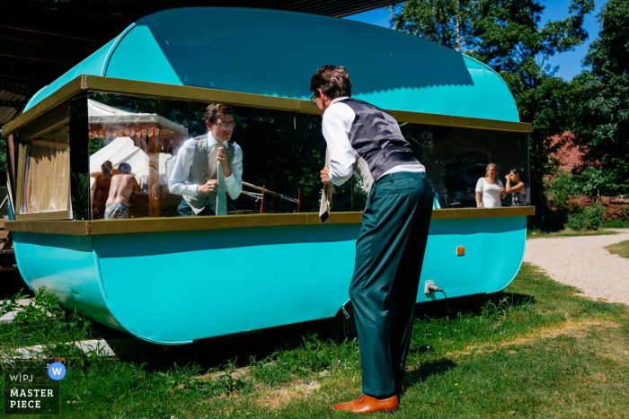 Le marié vérifie sa tenue dans un miroir de caravane, la mariée regarde au Camping de Lievelinge